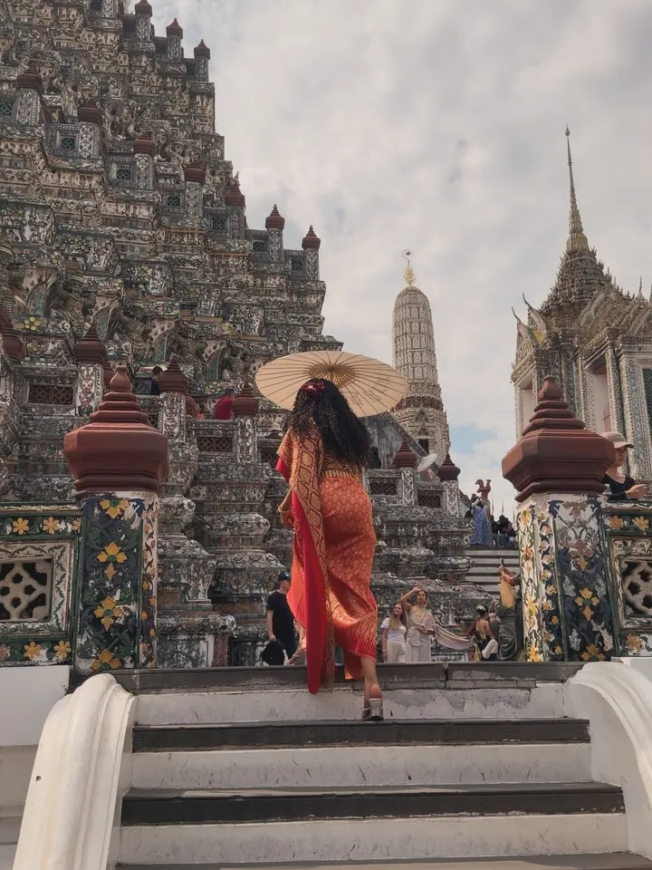 Kay walking up the steps of Wat Arun temple holding a paper parasol